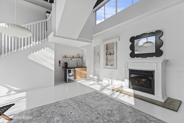 unfurnished living room featuring a high ceiling, wet bar, beverage cooler, and brick wall