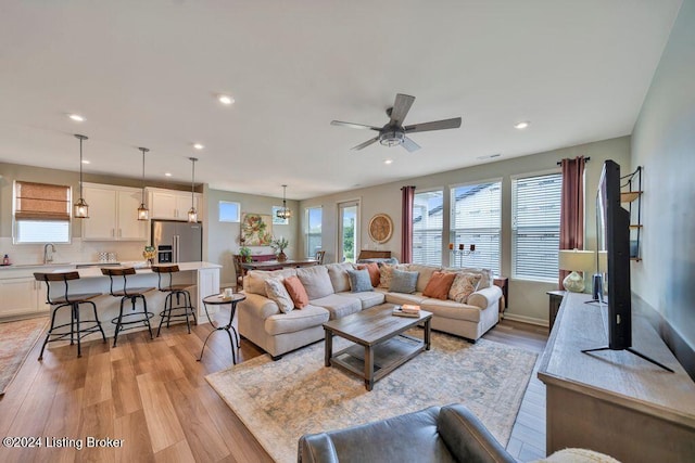 living room featuring ceiling fan with notable chandelier, light hardwood / wood-style flooring, and sink