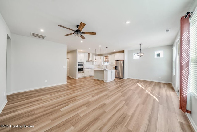 unfurnished living room with ceiling fan with notable chandelier, sink, and light hardwood / wood-style flooring