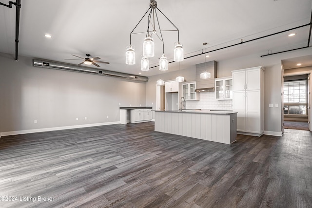 kitchen with dark wood-type flooring, white cabinetry, a center island with sink, and hanging light fixtures