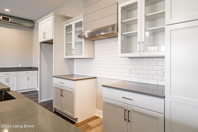 kitchen with dark stone counters, white cabinets, wall chimney range hood, dark hardwood / wood-style floors, and tasteful backsplash