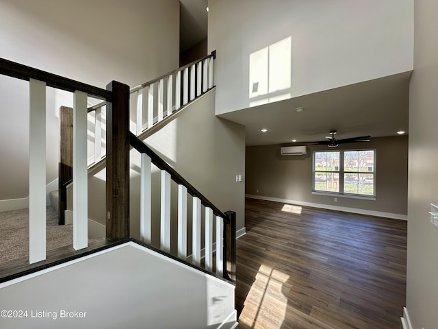 stairs with a wall mounted air conditioner, a towering ceiling, hardwood / wood-style flooring, and ceiling fan