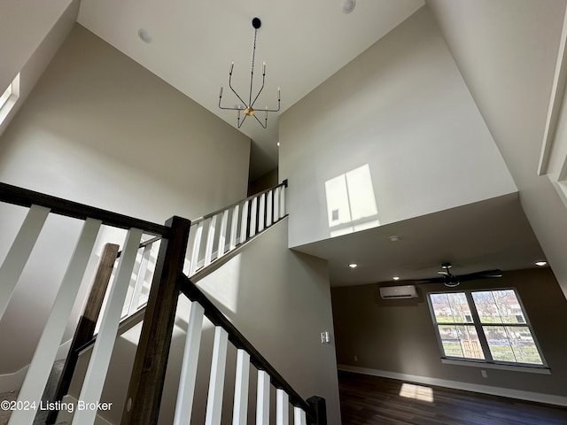 stairs featuring ceiling fan with notable chandelier, wood-type flooring, a towering ceiling, and a wall mounted air conditioner