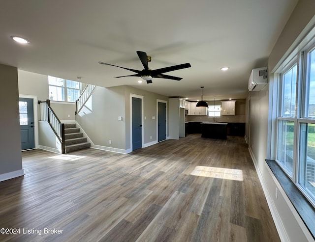 unfurnished living room featuring hardwood / wood-style flooring, an AC wall unit, and ceiling fan