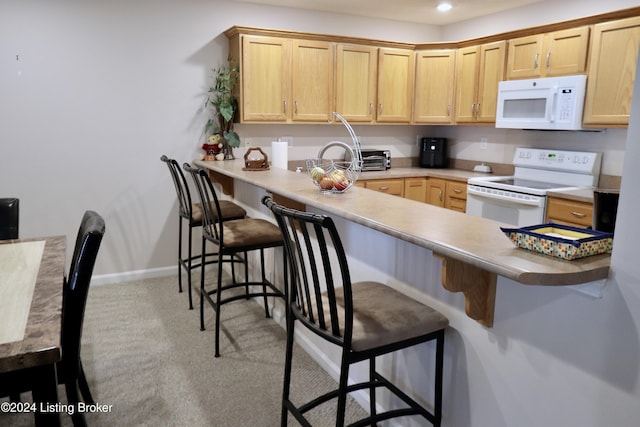 kitchen featuring kitchen peninsula, white appliances, light brown cabinetry, light carpet, and a breakfast bar