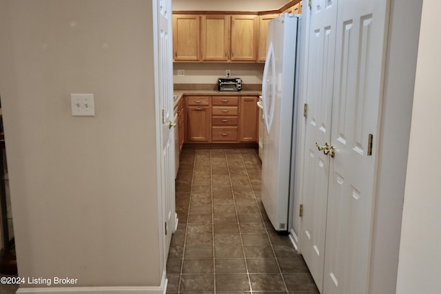 kitchen with light brown cabinetry, dark tile patterned flooring, and white refrigerator