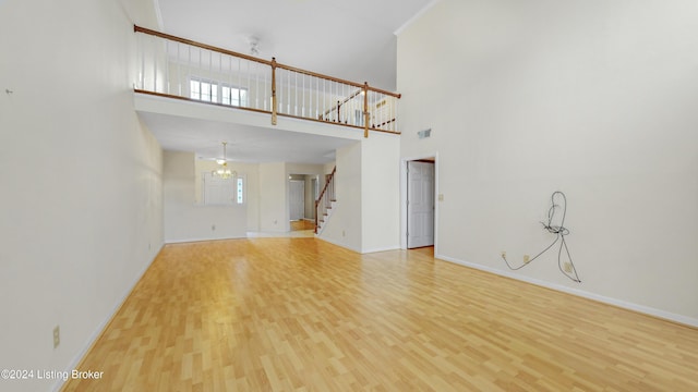 unfurnished living room with light hardwood / wood-style flooring, a towering ceiling, and a chandelier