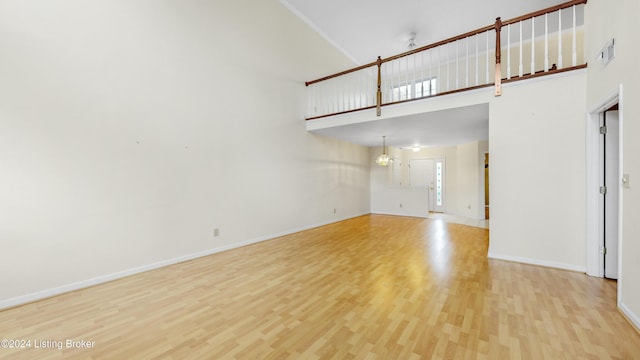 unfurnished living room featuring an inviting chandelier, a towering ceiling, and light wood-type flooring