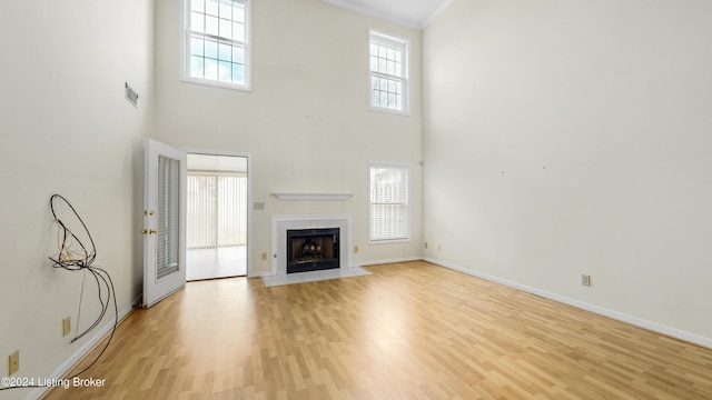 unfurnished living room with light hardwood / wood-style floors, a towering ceiling, crown molding, and a tile fireplace