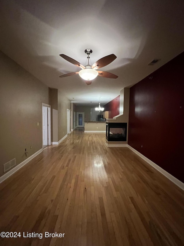 unfurnished living room with a multi sided fireplace, ceiling fan, and wood-type flooring