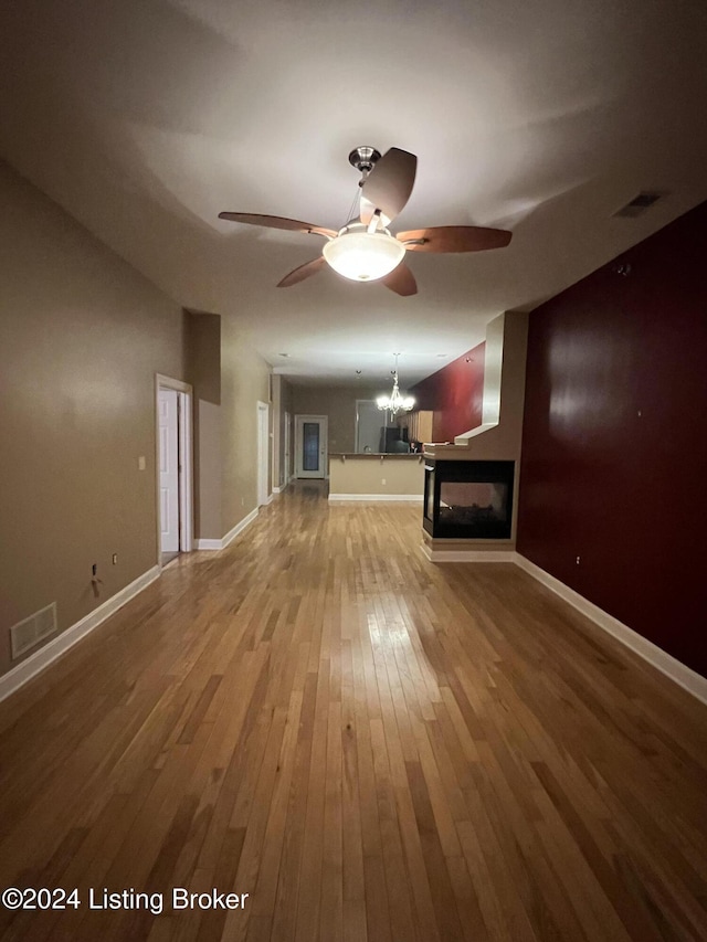 unfurnished living room featuring hardwood / wood-style floors, ceiling fan with notable chandelier, and a multi sided fireplace