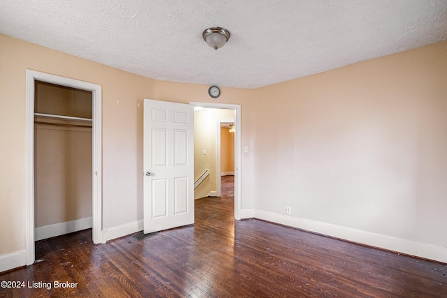 unfurnished bedroom with a textured ceiling, a closet, and dark wood-type flooring