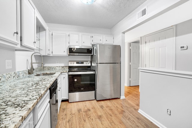 kitchen with light wood-type flooring, a textured ceiling, stainless steel appliances, sink, and white cabinetry