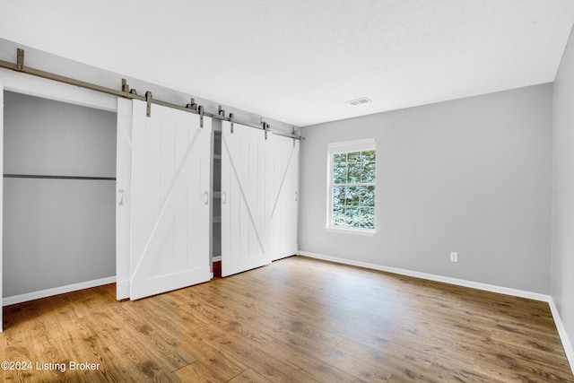 unfurnished bedroom featuring wood-type flooring and a barn door