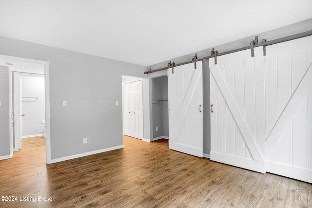 unfurnished bedroom with hardwood / wood-style floors, a barn door, and a closet