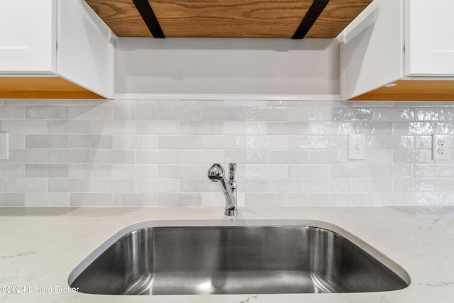 details featuring tasteful backsplash, white cabinetry, sink, and light stone counters