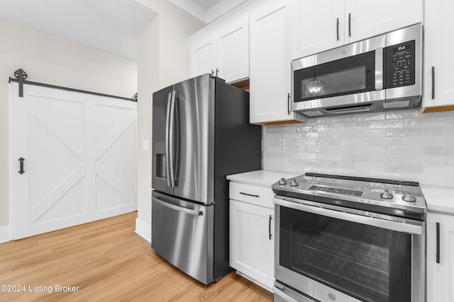 kitchen featuring white cabinets, a barn door, tasteful backsplash, light hardwood / wood-style floors, and stainless steel appliances