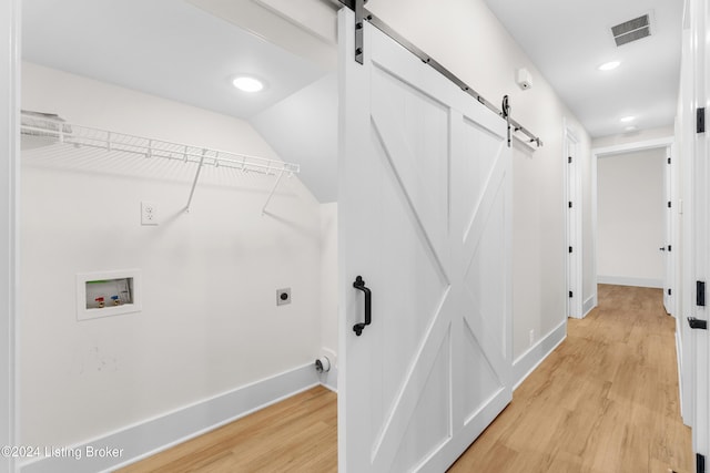 clothes washing area featuring a barn door, hookup for a washing machine, and light hardwood / wood-style floors