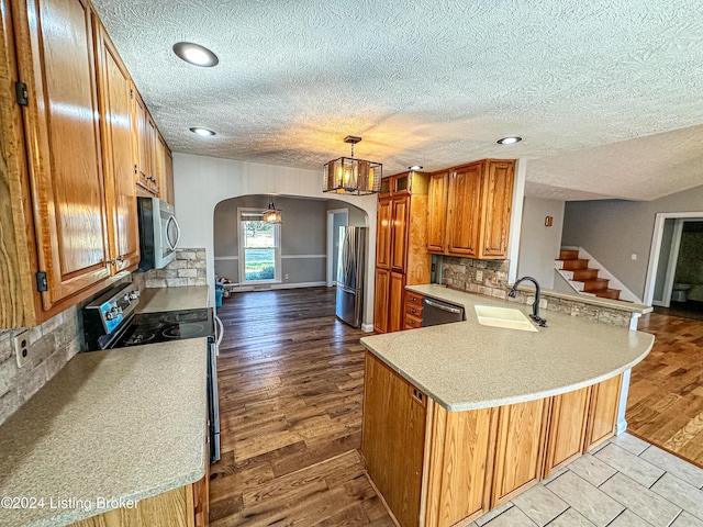 kitchen with sink, stainless steel appliances, kitchen peninsula, decorative light fixtures, and light wood-type flooring