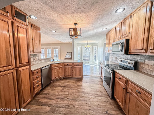 kitchen with sink, hanging light fixtures, dark hardwood / wood-style flooring, kitchen peninsula, and appliances with stainless steel finishes