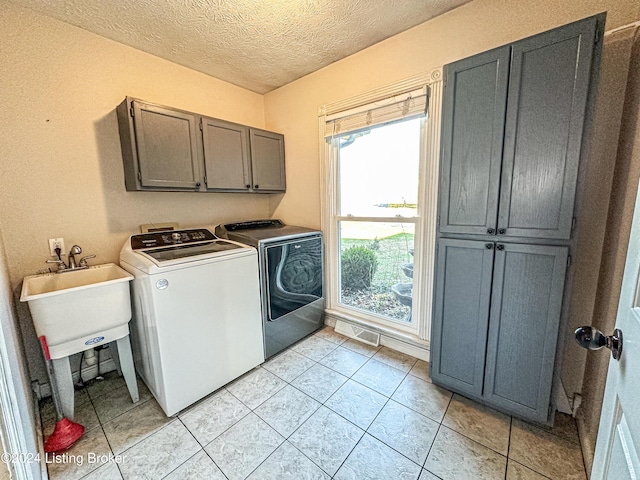 laundry room with cabinets, a textured ceiling, washer and clothes dryer, and light tile patterned flooring