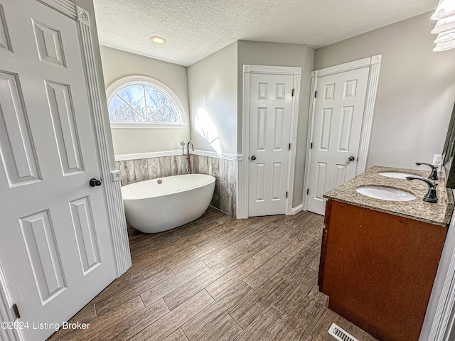 bathroom with vanity, wood-type flooring, a textured ceiling, and a tub to relax in