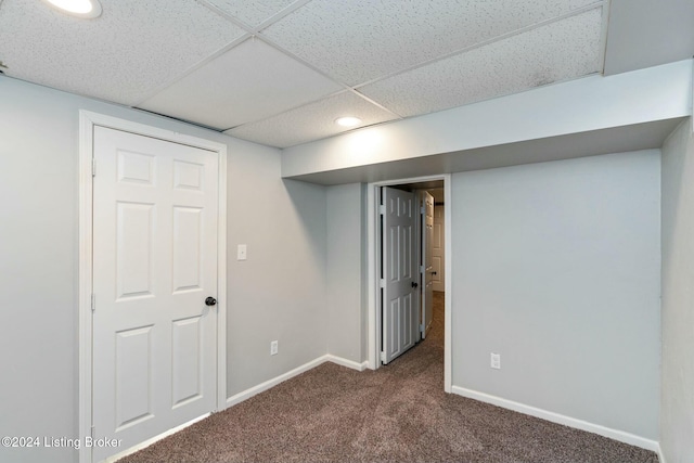 basement with a paneled ceiling and dark carpet