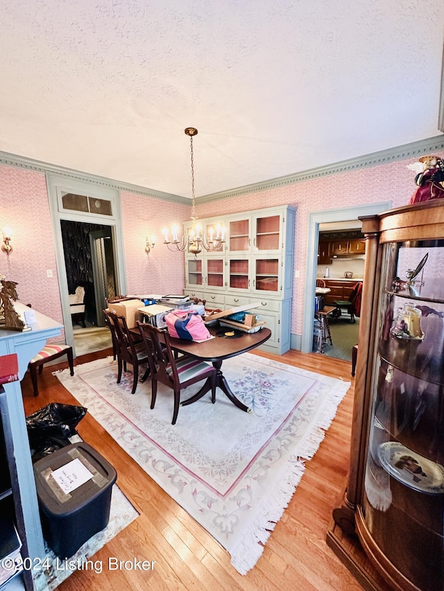 dining area featuring a notable chandelier, wood-type flooring, a textured ceiling, and ornamental molding