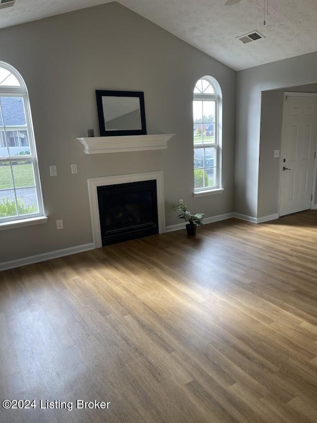 unfurnished living room featuring lofted ceiling, light hardwood / wood-style floors, and a textured ceiling