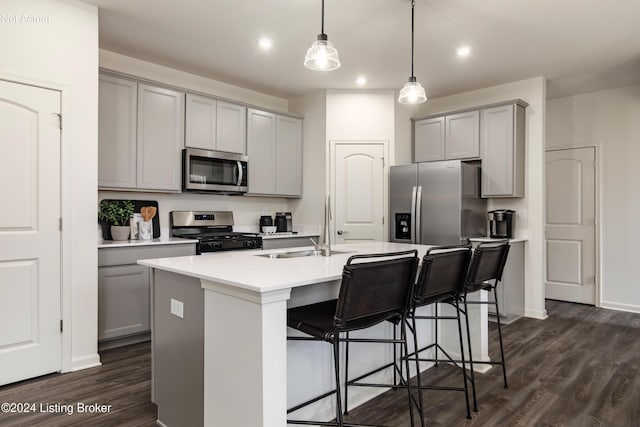 kitchen featuring gray cabinetry, a center island with sink, dark hardwood / wood-style floors, appliances with stainless steel finishes, and decorative light fixtures