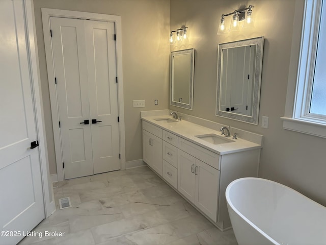 bathroom with marble finish floor, a freestanding bath, visible vents, and a sink