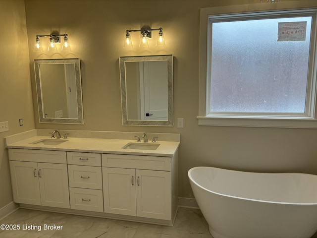 full bath with a freestanding bath, double vanity, a sink, and baseboards