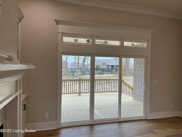 doorway with baseboards, crown molding, visible vents, and wood finished floors