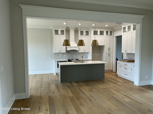 kitchen featuring wall chimney range hood, light wood-style flooring, a center island with sink, and crown molding