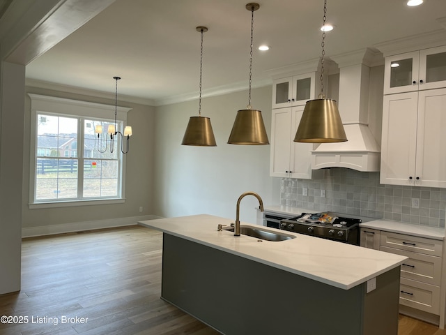 kitchen featuring tasteful backsplash, stove, crown molding, wall chimney range hood, and a sink