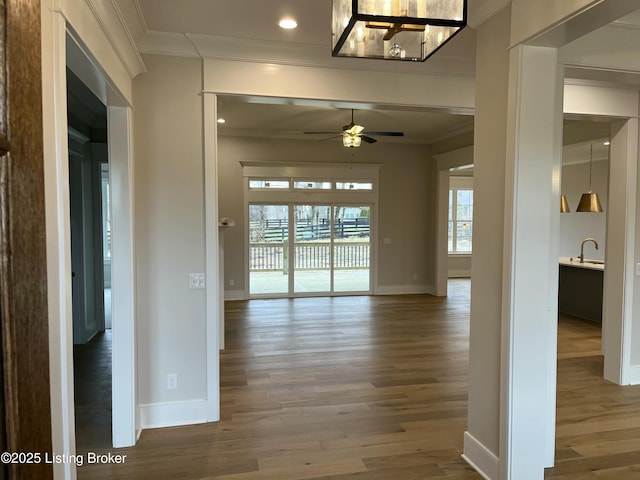 interior space with ornamental molding, a ceiling fan, baseboards, and wood finished floors