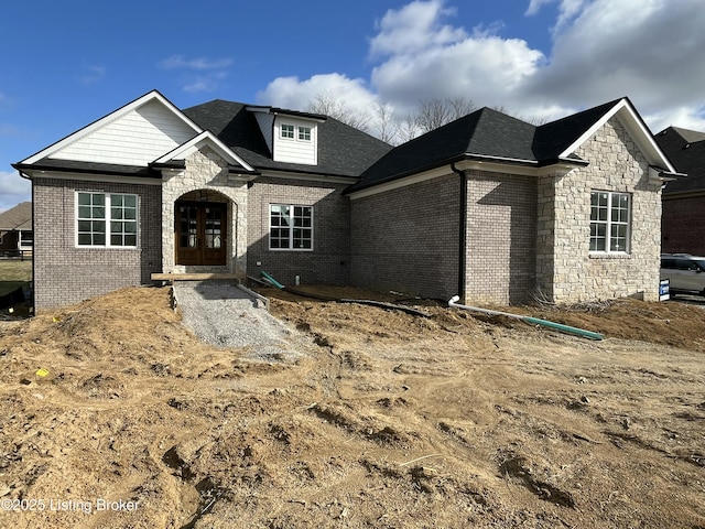 view of front of house with french doors, brick siding, stone siding, and a shingled roof