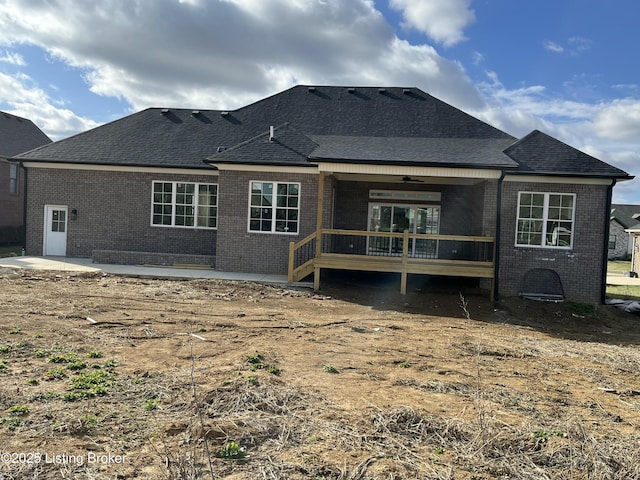 back of property with a wooden deck, a shingled roof, a patio, and brick siding