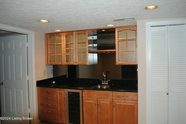 bar with a textured ceiling, sink, and beverage cooler