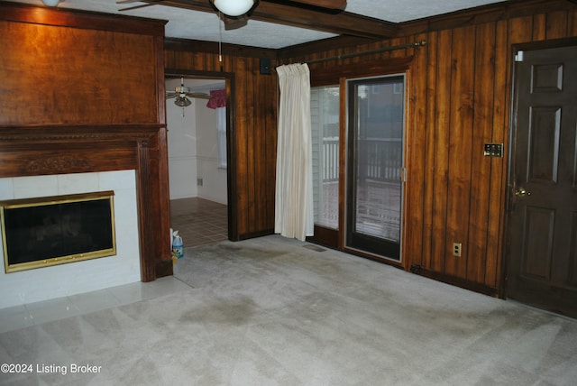 unfurnished living room featuring a tile fireplace, wooden walls, ceiling fan, beamed ceiling, and light colored carpet