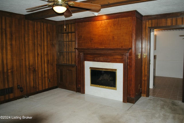 unfurnished living room with light carpet, ceiling fan, a tile fireplace, beamed ceiling, and wood walls