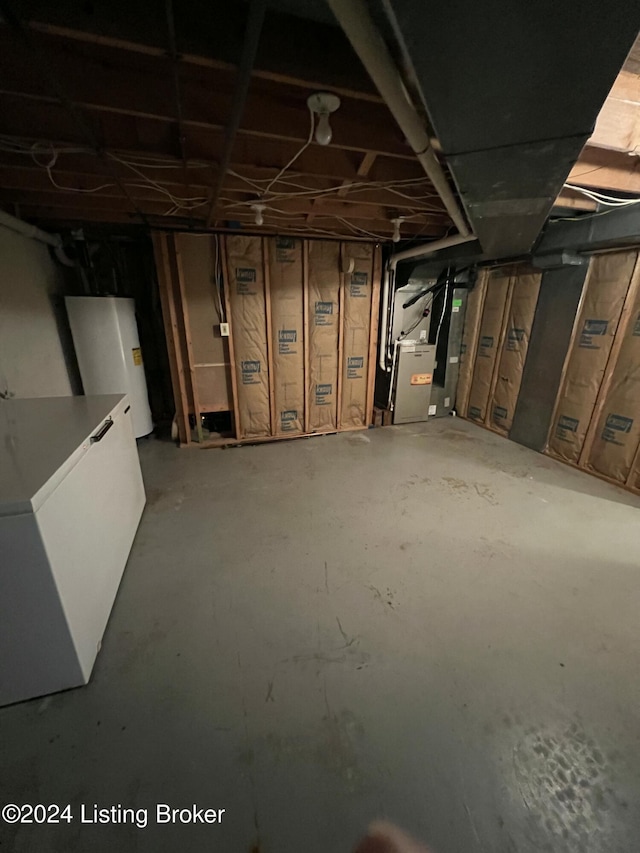 basement with white refrigerator, heating unit, and water heater