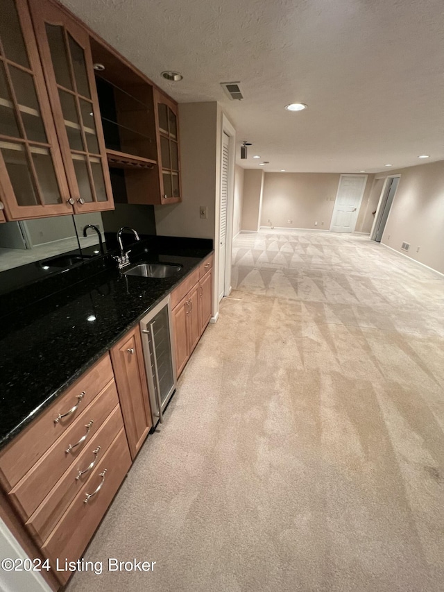 kitchen with dark stone counters, sink, light colored carpet, and a textured ceiling