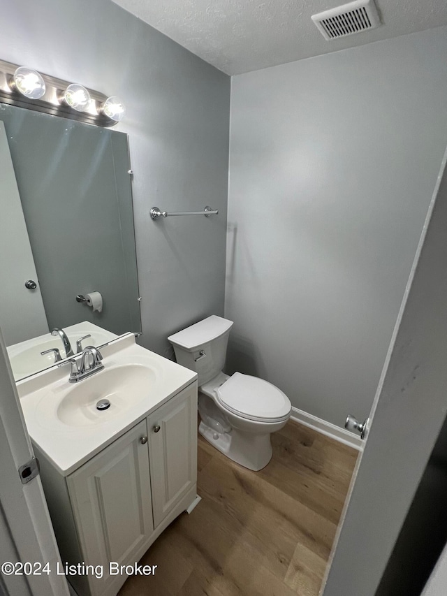 bathroom with wood-type flooring, toilet, vanity, and a textured ceiling