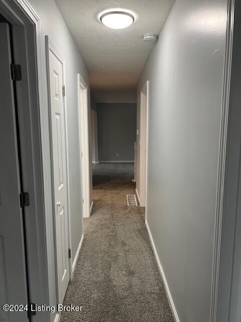 corridor with a textured ceiling and dark carpet