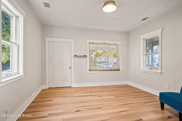 unfurnished room featuring a textured ceiling, light hardwood / wood-style flooring, and a healthy amount of sunlight