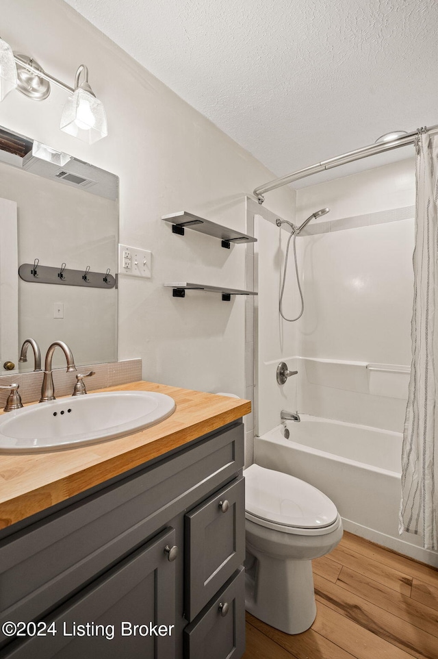 full bathroom featuring vanity, a textured ceiling, hardwood / wood-style flooring, shower / bathtub combination with curtain, and toilet