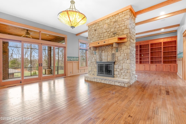 unfurnished living room featuring a fireplace, beam ceiling, light wood-type flooring, and ceiling fan