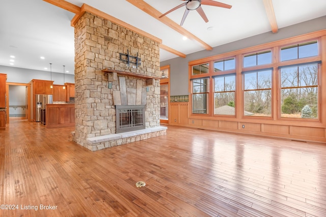 unfurnished living room featuring beamed ceiling, light wood-type flooring, a stone fireplace, and ceiling fan