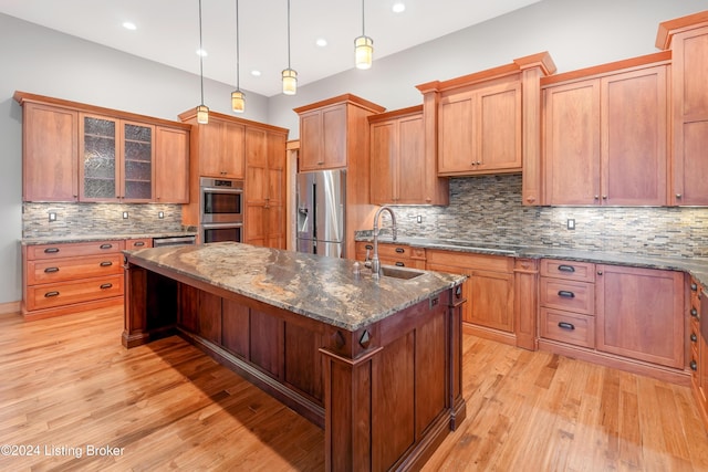 kitchen featuring a center island with sink, hanging light fixtures, sink, dark stone countertops, and appliances with stainless steel finishes